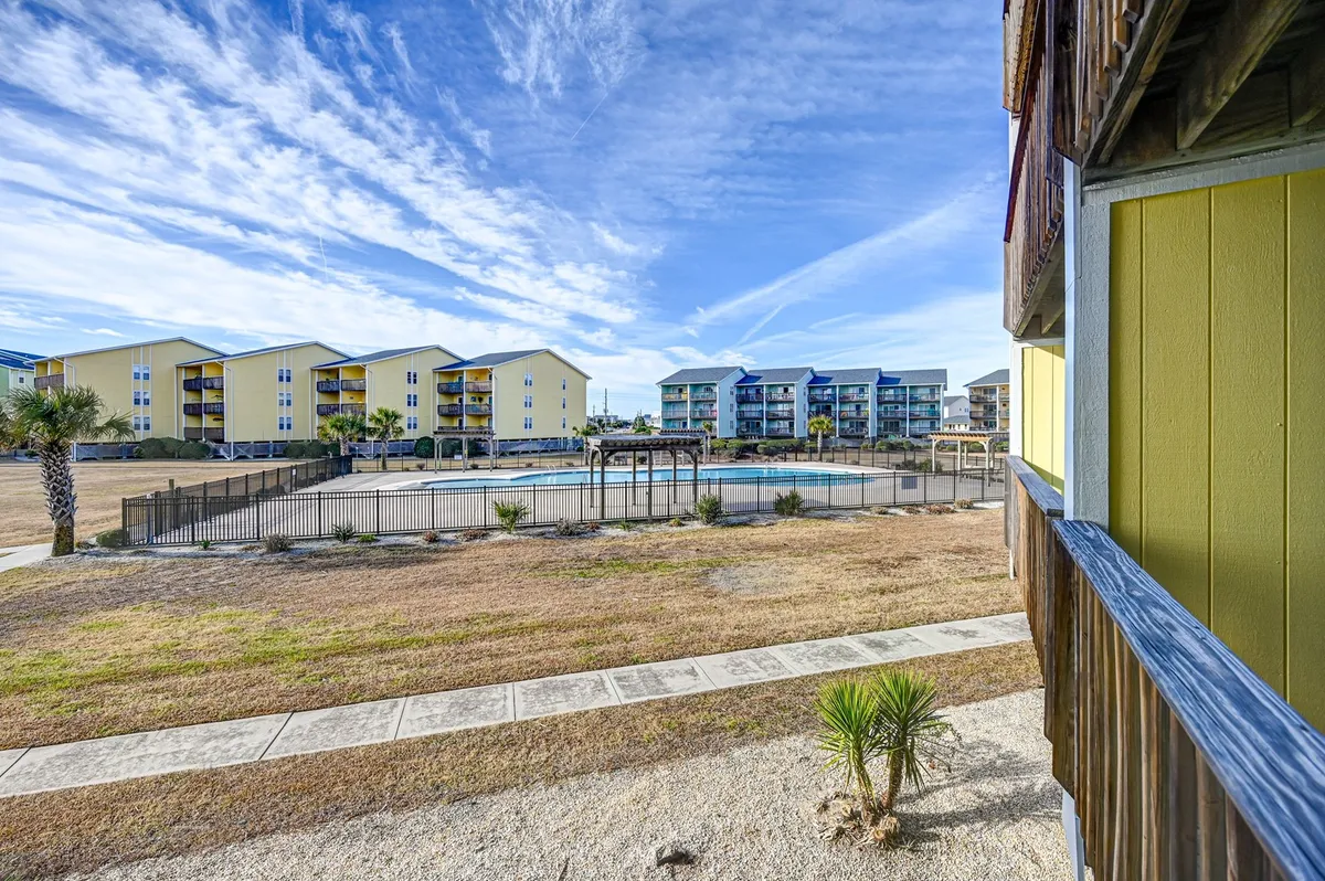 This image captures an inviting swimming pool surrounded by colorful buildings and palm trees. The area is well-lit, with guests able to relax poolside or enjoy a swim. The scene feels lively and summery, emphasizing social and recreational opportunities in the community.