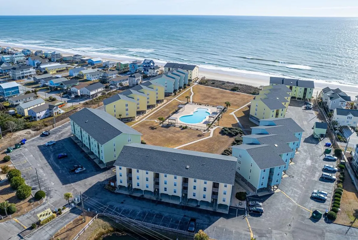 A serene exterior view featuring a swimming pool, surrounding residential buildings, and the ocean in the background. The scene is bathed in soft light, highlighting both the pool and the ocean horizon—perfect for capturing the tranquil views available from the porch.