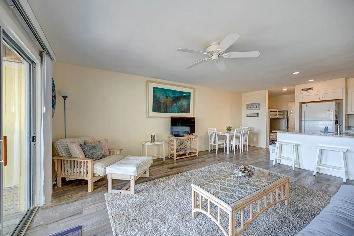 A cozy, open-plan condo interior featuring a comfortable sofa, coffee table, dining area, and artwork on the wall. The room is well-lit and arranged for relaxation or entertaining, highlighting the private and comfortable single-level living space.
