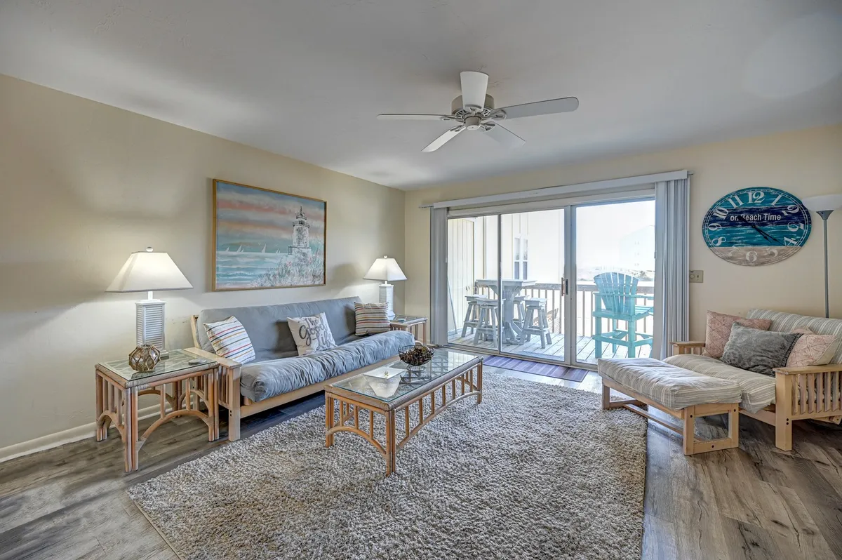 A cozy living room scene with a light-colored sofa and coffee table, tasteful wall art, and a clear view leading out to a balcony. The inviting setup suggests a space perfect for socializing, relaxing, and enjoying the view beyond the glass doors.