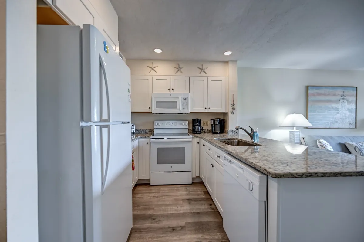 A well-lit kitchen space displaying a granite countertop, white cabinetry, and modern kitchen appliances. Decorative elements like a starfish and a cozy lampshade add warmth, while the open area hints at an environment perfect for cooking, entertaining, or casual family gatherings.