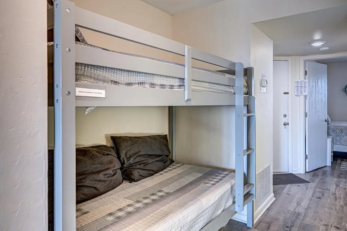 A hallway nook with a built-in bunk bed, plush pillows, and a nearby doorway. The compact, cleverly designed space offers a fun spot for kids or friends to sleep, maximizing comfort and flexibility in a small footprint.